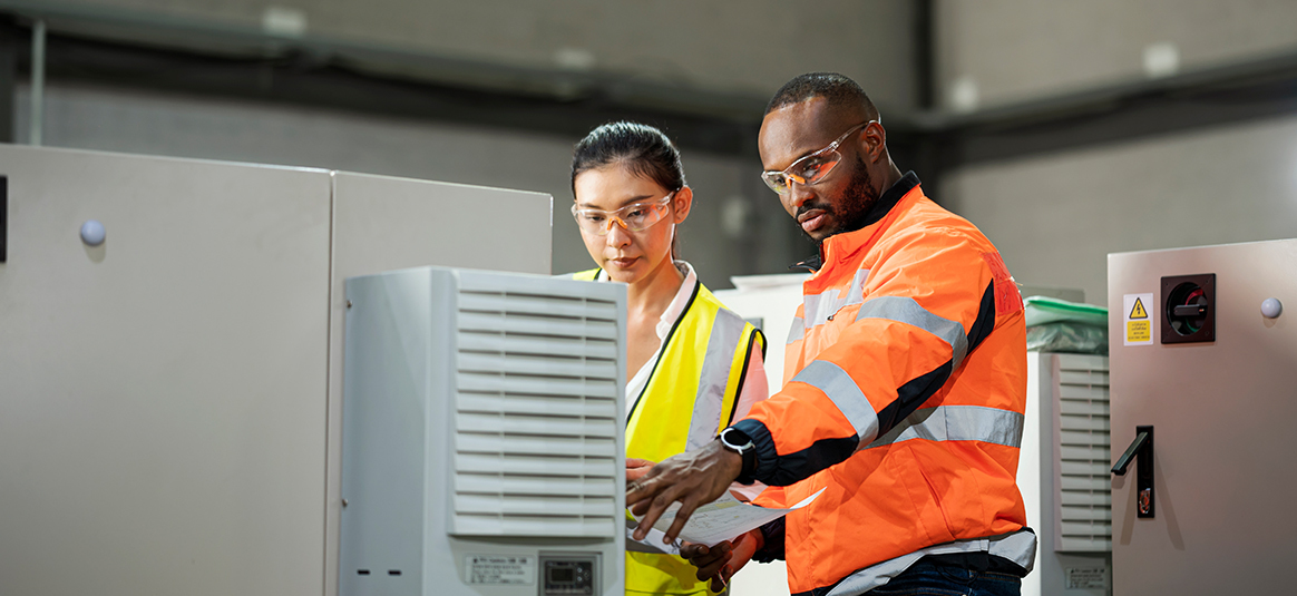 Two people wearing safety goggle and hi-vis jackets looking at a piece of machinery.