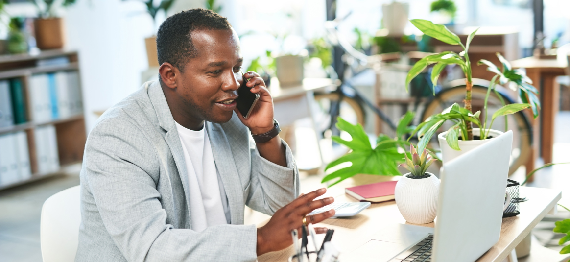 A man sitting at desk on mobile phone with laptop open