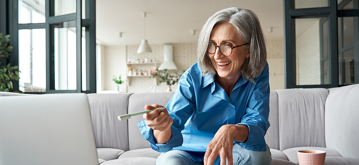 Photo of a smiling woman sitting on a sofa and pointing to an open laptop