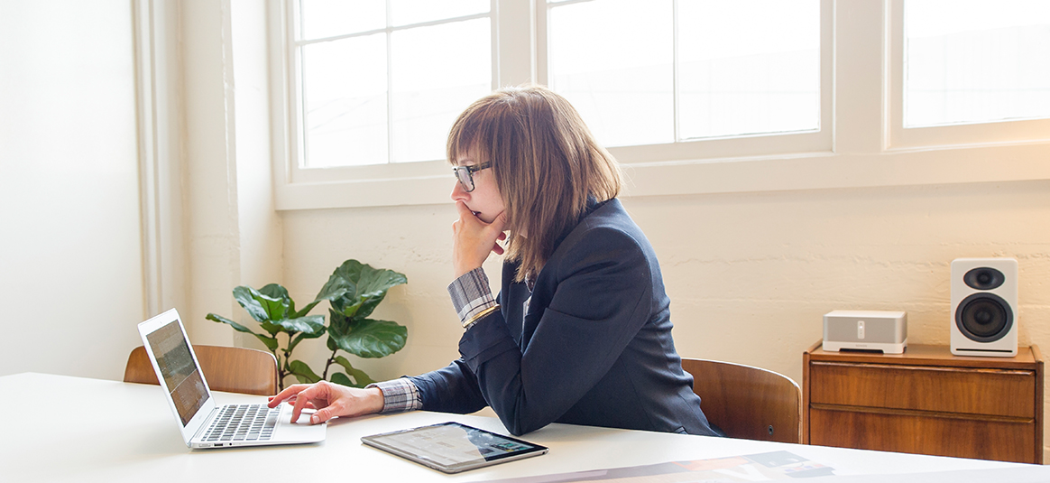 Business woman sitting at desk using laptop with a tablet to the side 