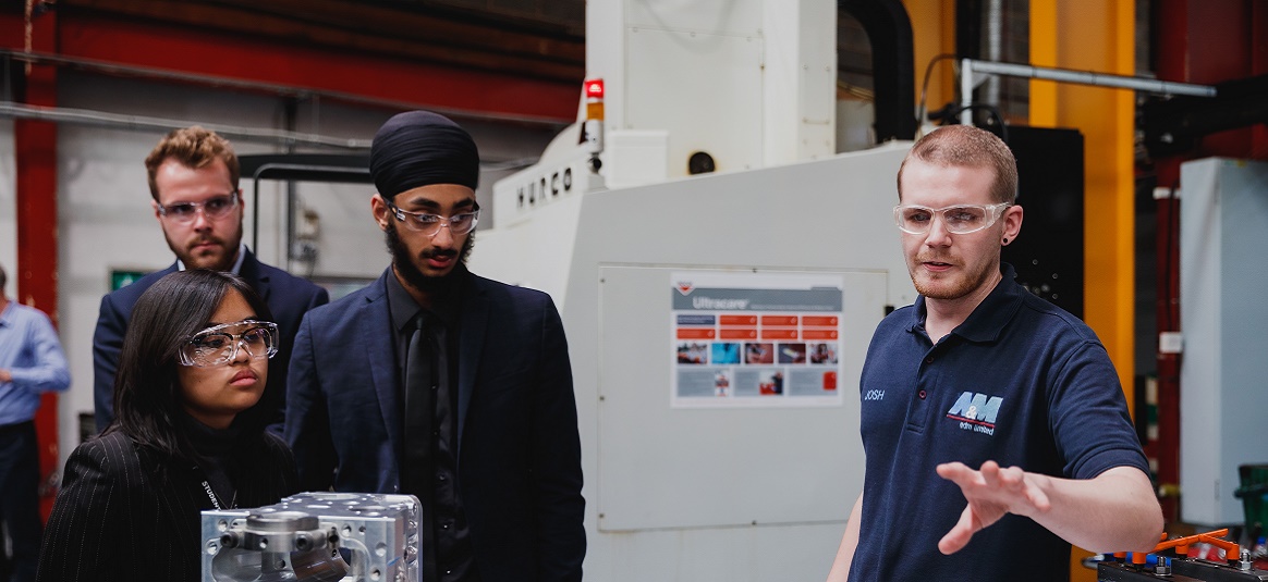 Three apprentice workers in safety goggles being shown around factory