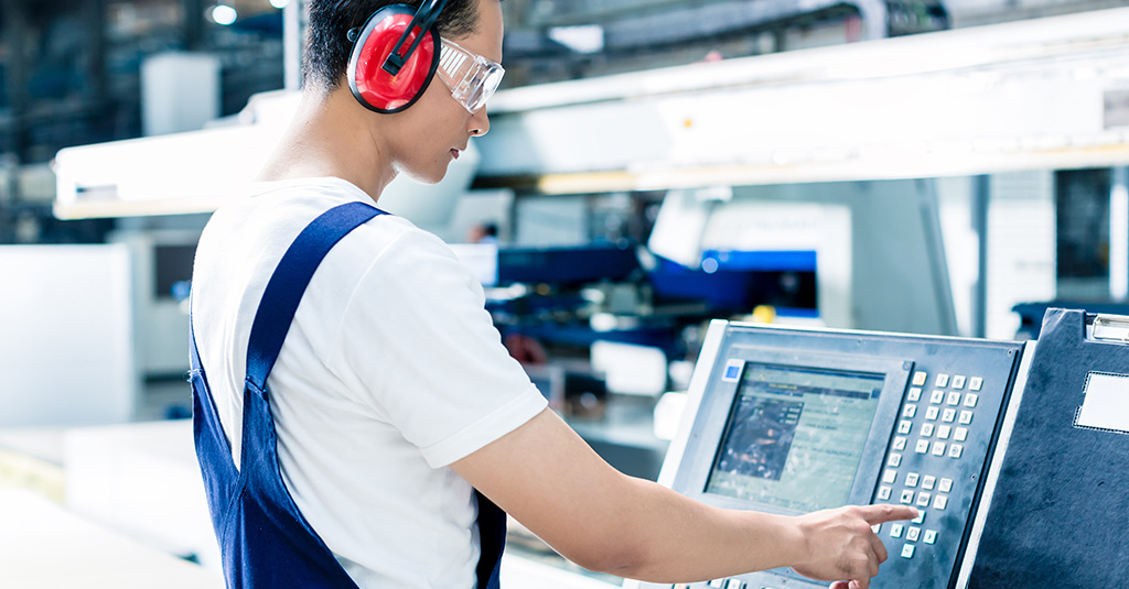 Photo of a person wearing PPE standing at a factory console.