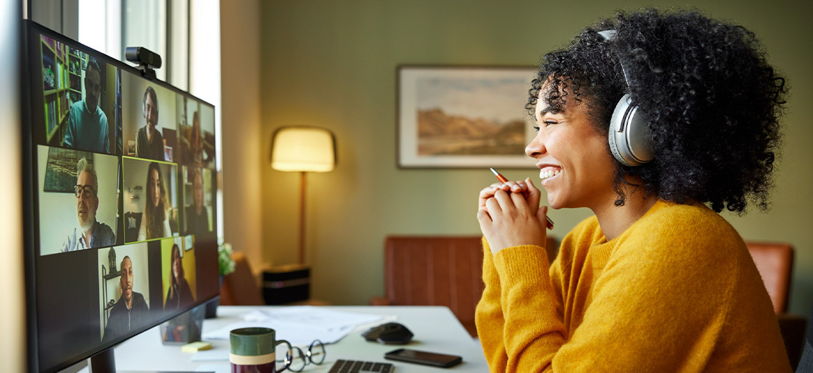 Photo of a smiling woman on a video conference at a home desk.