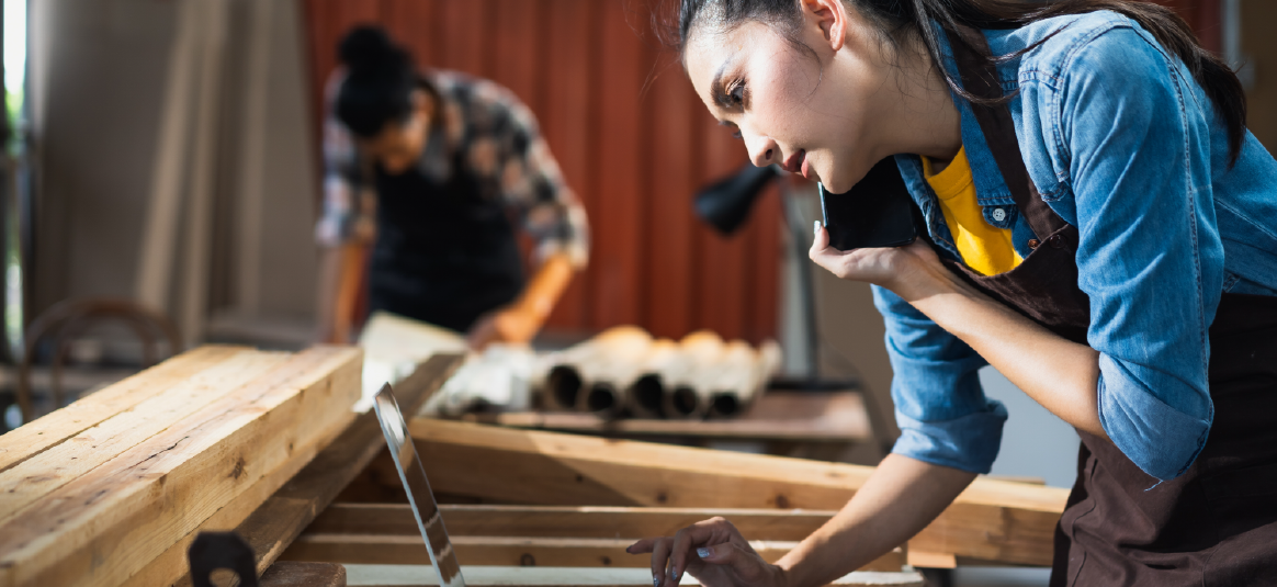 Photo of a person using a phone and a laptop in a workshop