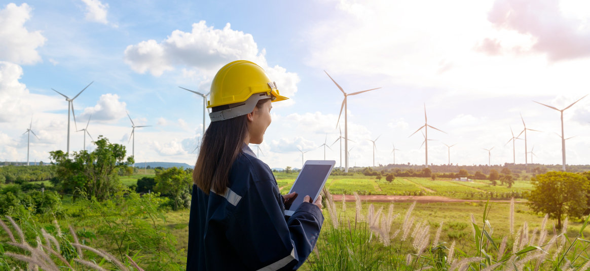 Photo of a worker with a tablet standing in front of a wind farm