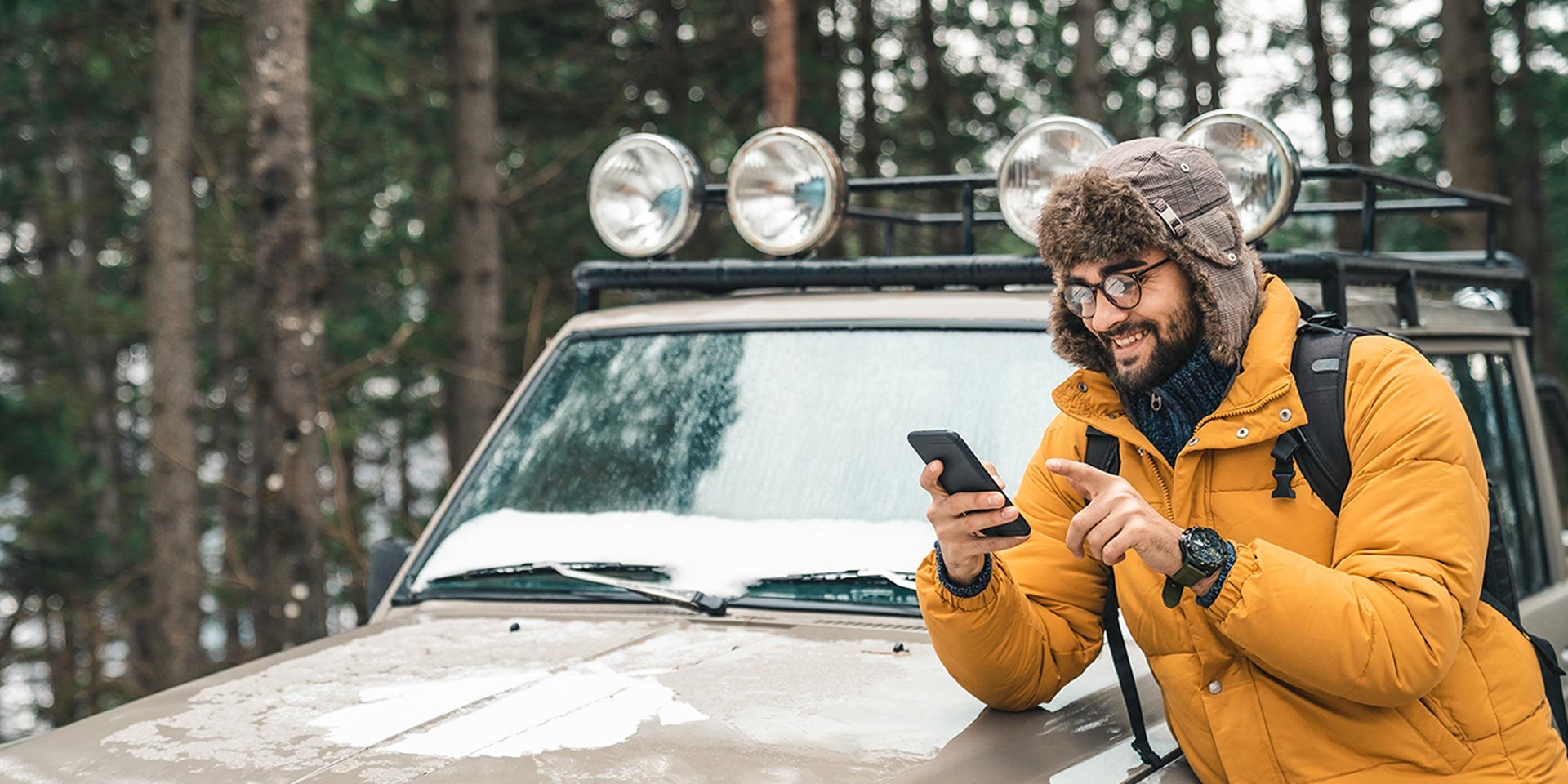 A man leaning on his car and checking his phone.